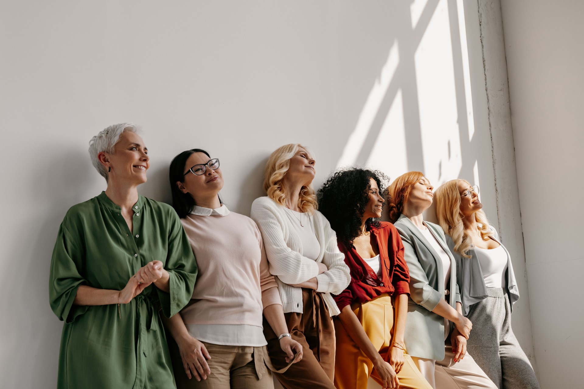 Multi-ethnic group of mature women bonding and smiling while leaning on the wall together